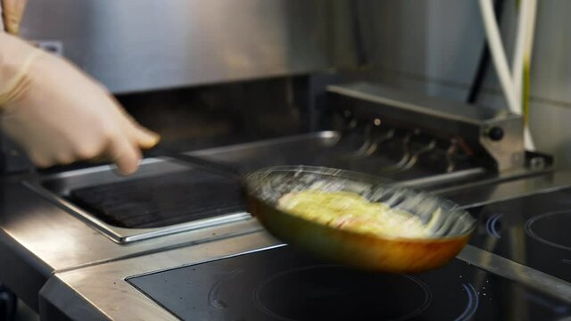 Cooking meals in a restaurant. Chef is cooking dish in a frying pan and flipping throwing it. Cooking the spaghetti in white sauce in the frying pan. Close-up.