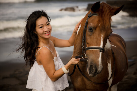 Portrait of smiling woman and brown horse. Asian woman cuddling horse. Romantic concept. Love to animals. Nature concept. Selected focus. Bali