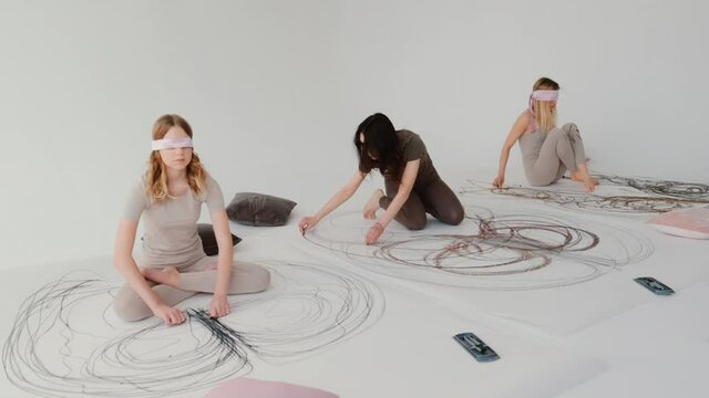 Girls paint an abstract picture with pastels during yoga, using their hands to draw. A light and airy creative studio with large canvases on the floor.