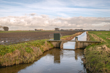 Small weir in a ditch in a Dutch polder. The weir is operated from a distance by the water board. The photo was taken in the province of Noord-Brabant on a slightly cloudy day in the winter season.