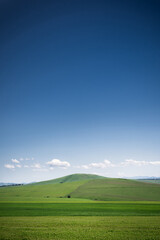 Beautiful landscape with green meadows on the hill, blue sky with clouds and mountains on the horizon. Farmland, summer day in nature, travel, idyll concept.