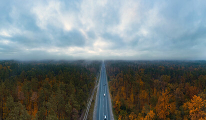 Highway road in autumn forest with dark moody sky with clouds from aerial view.