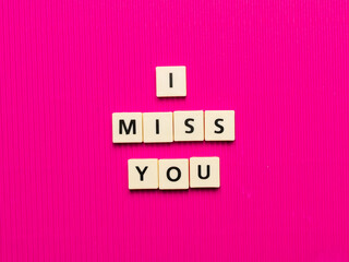 I MISS YOU word made from square letter tiles on pink background.