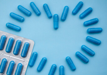 Blue medical capsules are laid out in the shape of heart and blister on blue background. Medical flat lay. Valentine's Day. World Pharmacist's Day