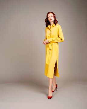 Gorgeous ginger woman in yellow shirt dress. Female bright look. Trendy trench and red high heel shoes at neutral studio background. Inner life concept.