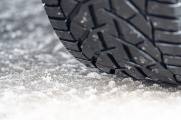 Close up winter tire of a car on the road covered by snow and ice driving in extreme cold temperature