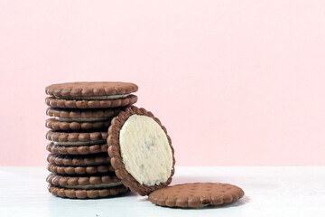 There's a stack of chocolate chip cookies on the table. Next to it is a broken cookie. The background color is pastel pink.