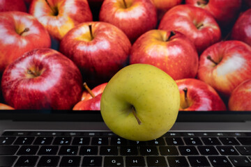 Real yellow apple on the laptop in front of a screen with red apples