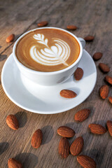 Coffee almond milk in a white mug and almond kernels on the table.