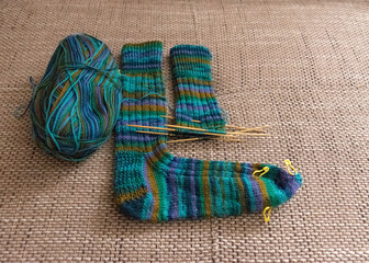 Fototapeta na wymiar knitted sock knitted with green striped yarn, wooden knitting needles and a ball of wool yarn, handicrafts as a hobby, knitting concept