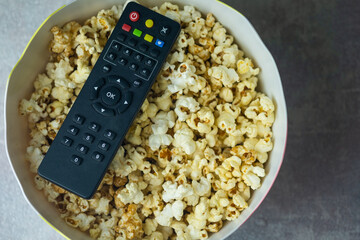 Black TV remote on popcorn in bucket.