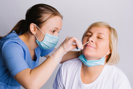 A young doctor in a medical mask takes a COVID 19 test, nasal swab from an elderly woman against a white background. Virus detection concept.