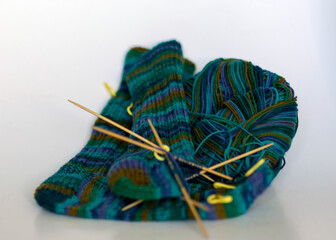 knitted sock knitted with green striped yarn, wooden knitting needles and a ball of wool yarn,...