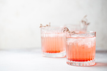 Cold fresh pink lemonade drink with ice in a glass on white background, selective focus