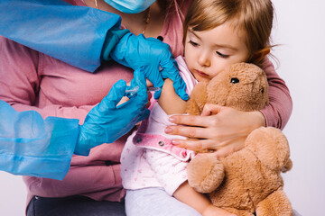 The girl looks at the syringe with fear. The doctor's hands are injected into the forearm. Vaccination for covid 19.