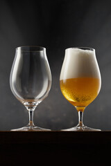 A full glass of light beer and an empty glass on a dark background