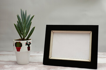 Small potted plant decorated with blank frame on the side on wooden base and gray background