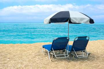 Empty Beach with two lounge chairs and beach umbrella. Azure blue water and amazing sky.
