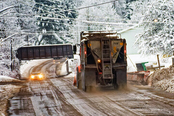 Fototapeta na wymiar A snow plow truck is heading toward a narrowing of the road as it approaches the train overpass as two cars are heading in opposite direction. Small town of Windsor in Broome County in Upstate NY.