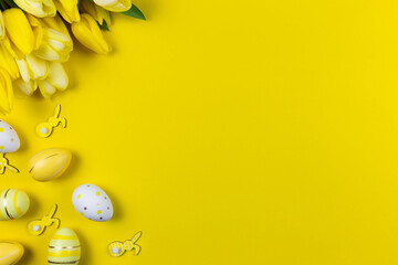 Beautiful yellow tulips with colorful easter eggs and bunnies on yellow background. Spring and Easter holiday flat lay. Top view. Copy space.