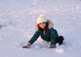 Fototapeta na wymiar Little pretty girl wearing winter clothes playing on the snow alone looking at camera