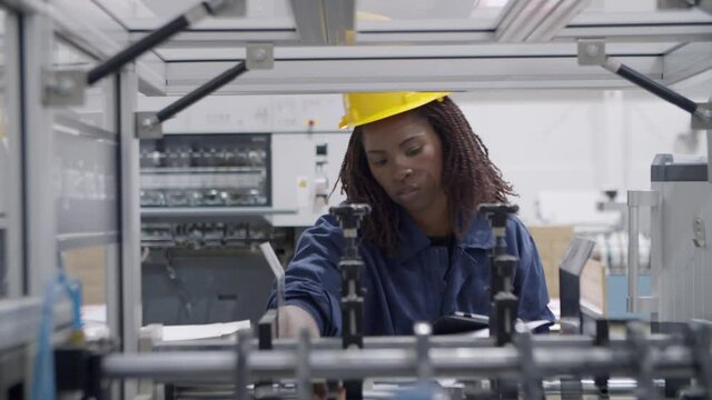 Focused young black female factory worker studying and testing new industrial machine with paper manual. Production or machinery concept