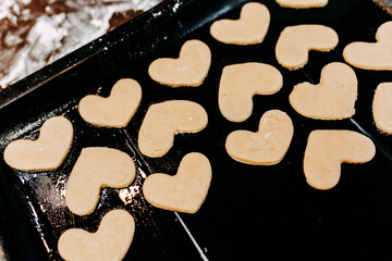 Cookies in shape of heart for the Saint Valentine's Day. Dough, flour, baking pan, round wooden cutting board and rolling pin on the table.
