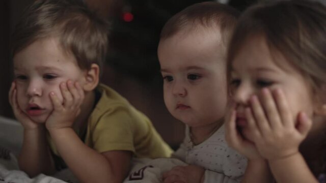 Family, leisure, childhood, friendship concepts - authentic three young preschool toddler minor children kids siblings watch cartoon on smartphone phone device together on sofa in room at home indoors