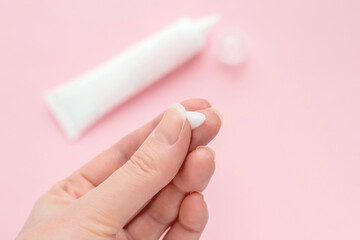 Female hand with a drop of cream on a finger. tube of cream isolated on a pink background....