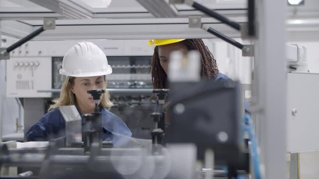 Black female factory engineer teaching middle aged employee to operate new industrial machine, using tablet and paper manual. Production process or machinery concept