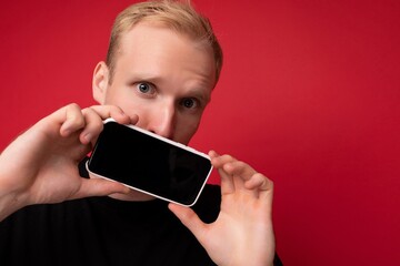close up photo of Handsome happy cool young man good looking wearing casual stylish clothes standing isolated over colourful background wall holding smartphone and showing phone with empty screen