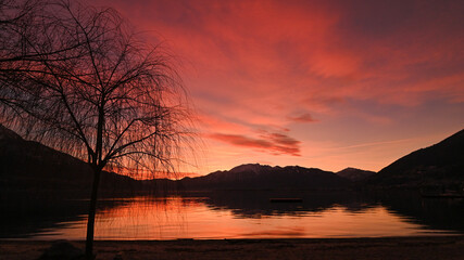 Favoloso tramonto sul lago, con nuvole arancioni e rosse che si riflettono nell'acqua del lago © fotonaturali