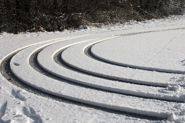 High angle shot of concentric tire tracks of a car in the snow near the road