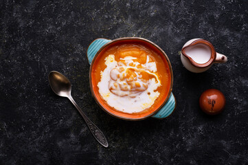 baked pumpkin cream coup with  coconut milk served in nice bowl at wooden black table. flat lay. cooking and healthy life concept