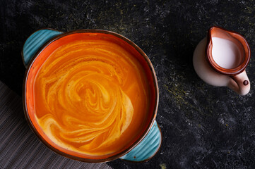 baked pumpkin cream coup with  coconut milk served in nice bowl at wooden black table. flat lay. cooking and healthy life concept