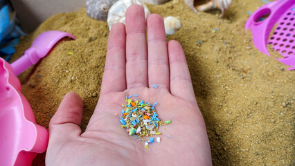 Top view of a person holding microplastics in his hand. Nonrecyclable materials. Selective focus with shallow depth of field. Holding microplastics from the sand on the beach.