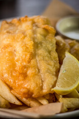 Classic crispy deep fried fish and chips with lemon and tartar sauce white dish on a wooden table