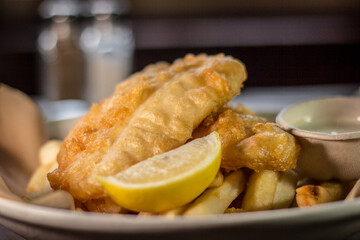 Classic crispy deep fried fish and chips with lemon and tartar sauce white dish on a wooden table