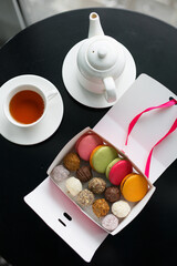 set of truffles and cookies in a box on a table against the background of a teapot