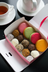 set of truffles and cookies in a box on a table against the background of a teapot