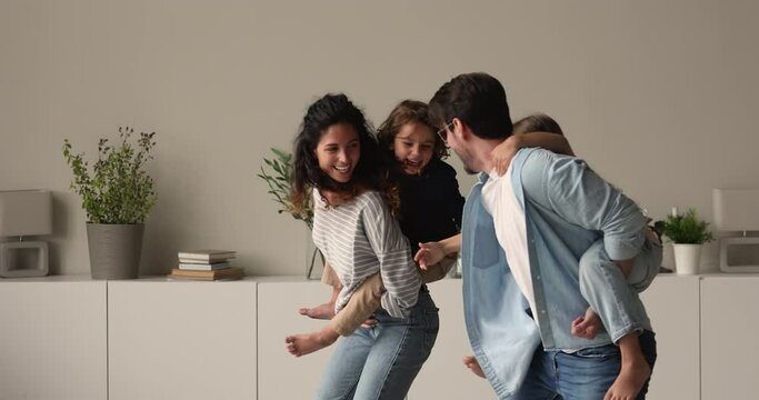 Family with preschool kids playing in living room, mom and dad carrying son and daughter running catching each other having fun enjoy active weekend at modern flat. Leisure activity at home concept