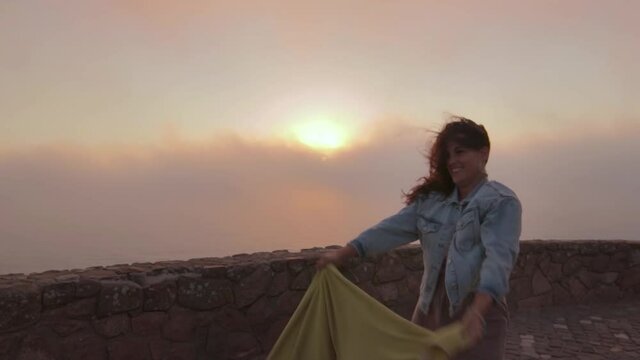 mujer bailando alegre al atardecer con mucho viento en un acantilado de Cabo da Roca, Portugal.