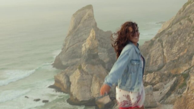 mujer bailando alegre al atardecer con mucho viento en un acantilado de Cabo da Roca, Portugal.