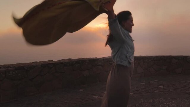 mujer bailando alegre al atardecer con mucho viento en un acantilado de Cabo da Roca, Portugal.