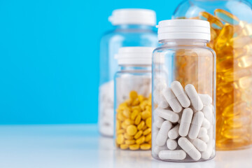 White gel capsules scattered on white surface. Orange pills in bottle blue background. Nutritional Supplements, Vitamins. Omega 3, multivitamins, Calcium, antibiotics. Health. Immunity