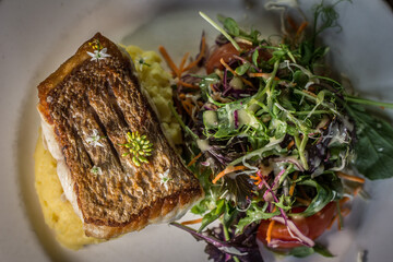 Gourmet garnished grilled salmon with salad mash potato on a white dish wooden table