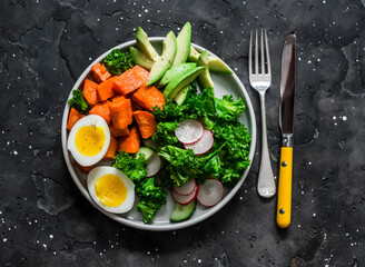 Vegetarian lunch - boiled sweet potatoes, egg, kale, avocado, radish, cucumber salad on a dark background, top view
