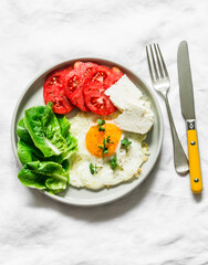 Delicious breakfast, snack, tapas - fried egg, ripe tomatoes, greek cheese, green salad on a light background, top view