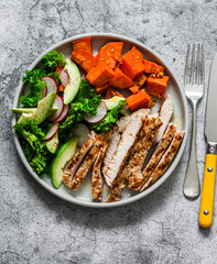 Balanced diet food - grilled turkey, sweet potatoes, kale cabbage, avocado, cucumbers, radish salad on a grey background, top view