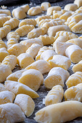 Gnocchi preparation steps: Raw uncooked handmade gluten free potato gnocchi on a dark table with sprinkled flour on top. Creating authentic pasta dough for an Italian dish. Side view.